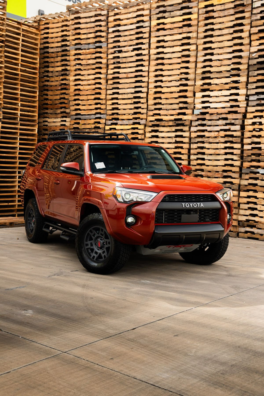 Orange Toyota 4Runner with a roof rack in front of stacked pallets