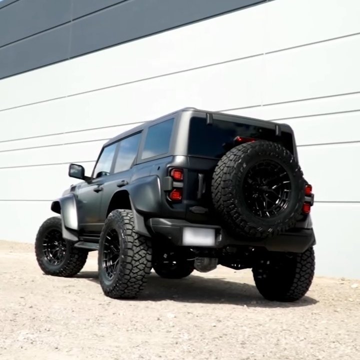 Black Ford Bronco on large off-road tires parked beside a white building