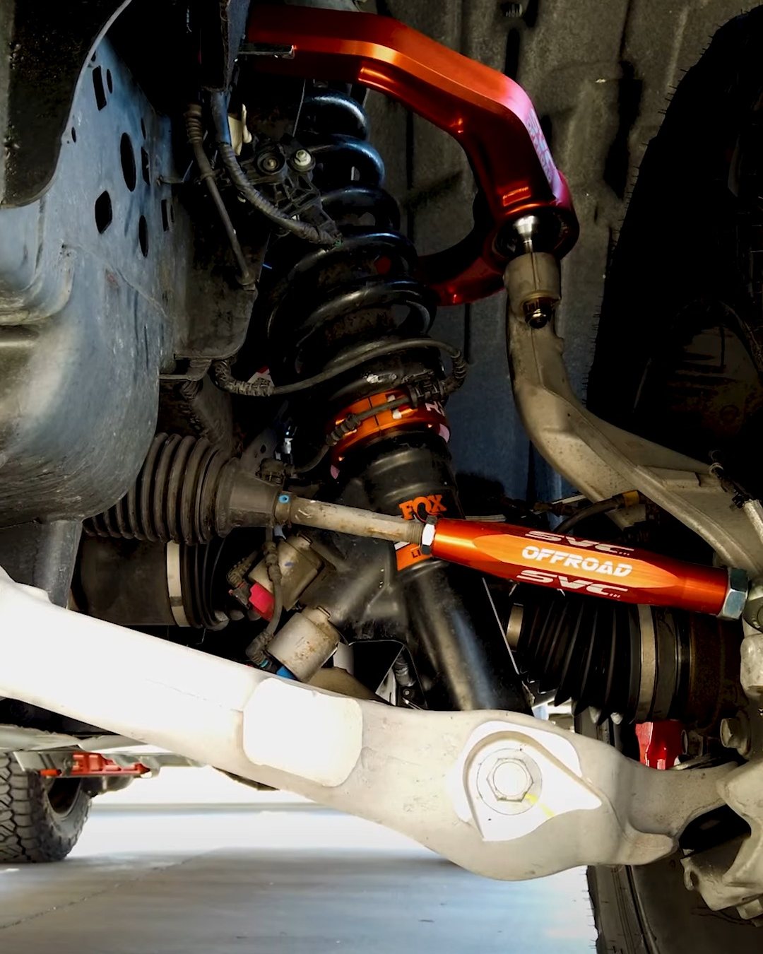 Aftermarket coilover and orange upper control arm installed on a truck front suspension