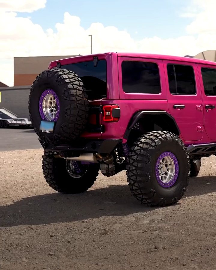 Lifted pink Jeep Wrangler on large off-road tires parked on a dirt lot