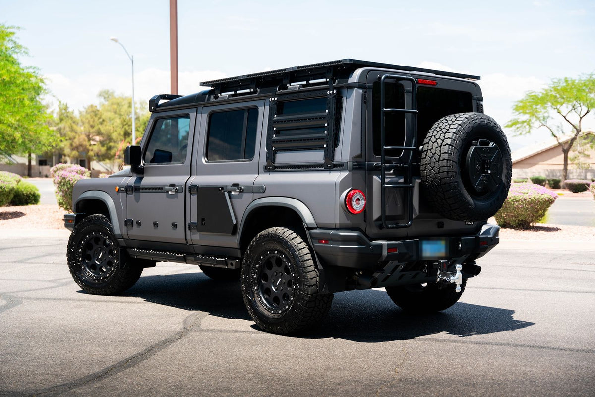 Grey INEOS Grenadier with a roof rack and ladder, rear three-quarter view