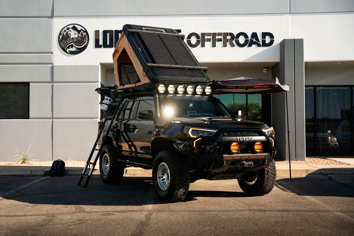 Black Toyota 4Runner with a rooftop tent and light bar parked under the Lone Wolf Off Road sign in Henderson