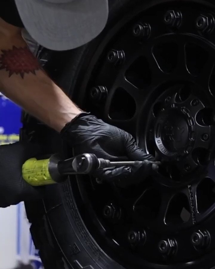 Technician tightening the lug nuts on a black off-road wheel